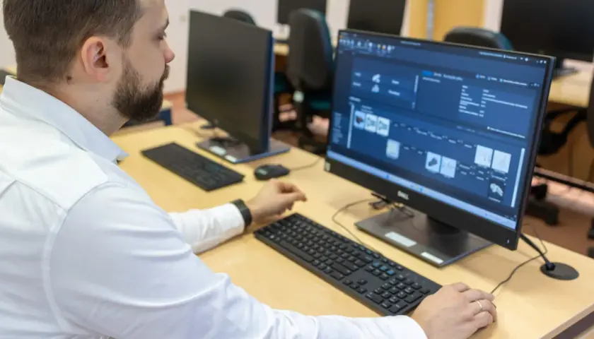 Mężczyzna w białej koszuli pracuje przy komputerze, analizując dane produkcyjne. To przykład nowoczesnego zarządzania i inżynierii produkcji.