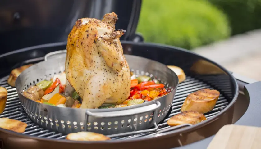 Un poulet rôti sur un barbecue, avec des légumes colorés et des tranches de pain grillé. Le poulet est assaisonné et semble juteux, prêt à être dégusté.