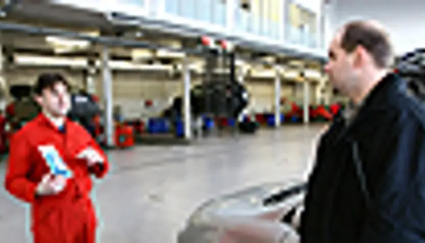 Mechanik w czerwonym kombinezonie omawia z klientem kwestie związane z ekologicznym paliwem, takim jak biodiesel, w warsztacie samochodowym.