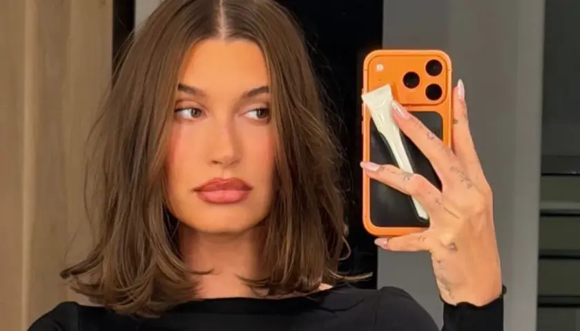 En kvinna med fina hårfrisyrer tar en selfie med sin orangea mobil.
