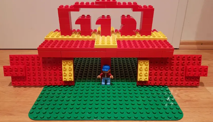Ein kleiner Junge steht unter einem roten und gelben LEGO Duplo Tor, das wie eine Feuerwache aussieht. Die Zahl 112 ist darauf abgebildet.