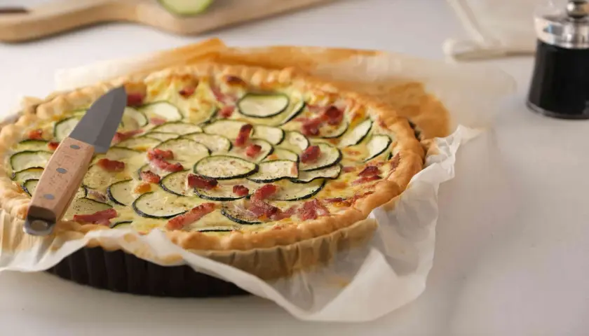 Une délicieuse quiche courgette lardon dorée, garnie de rondelles de courgettes et de lardons croustillants, prête à être dégustée.
