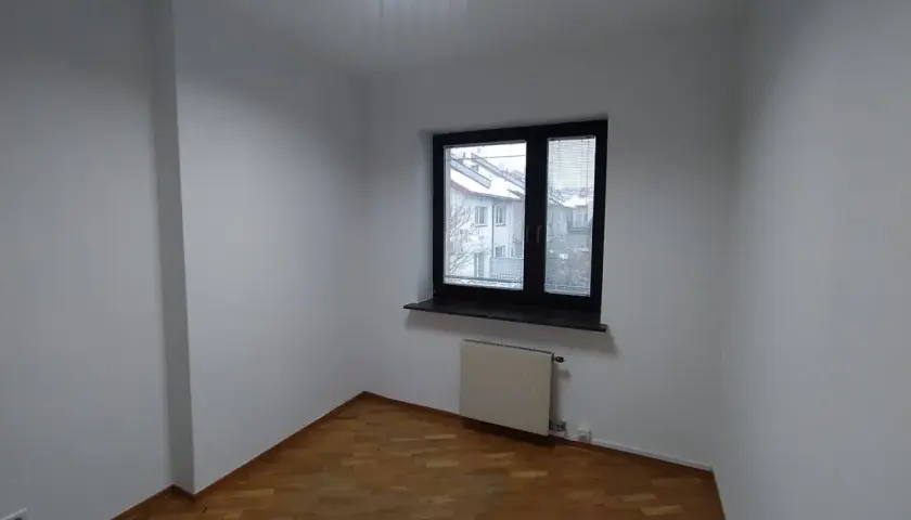Puste pomieszczenie z drewnianą podłogą i oknem. Zastanawiasz się, ile trwa malowanie mieszkania?