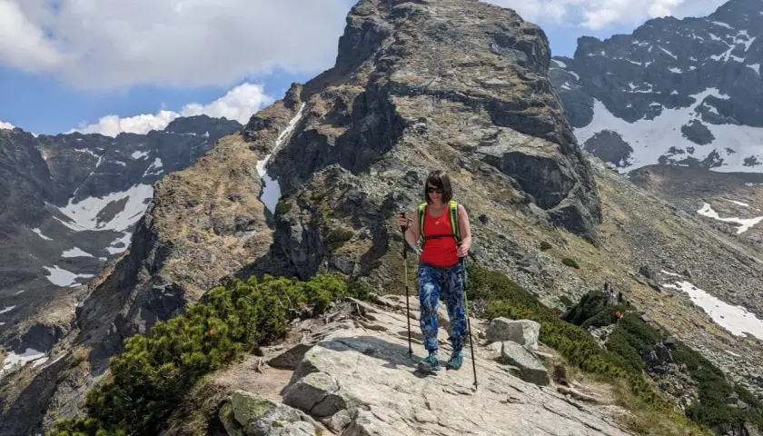 Kobieta z kijkami trekkingowymi na skalistej ścieżce w Dolinie Gąsienicowej. W tle majestatyczny szczyt i ośnieżone zbocza.