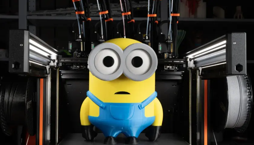 Minion wydrukowany na dobra drukarka 3d. Maszyna z wieloma głowicami i szpulami filamentu w tle.