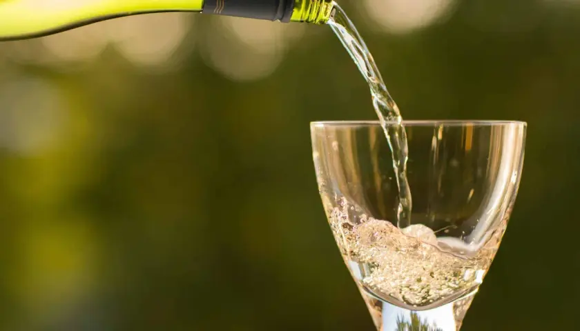 Un vin blanc pétillant est versé dans un verre, créant une mousse légère qui rappelle le sucre dans le vin.