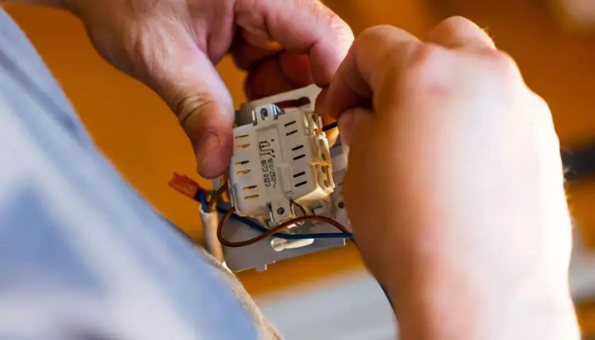 Ręce elektryka podłączają przewody do mechanizmu gniazdka. To kluczowy etap prac, wpływający na koszt instalacji elektrycznej.