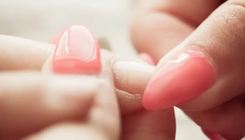 Zbliżenie na dłonie, gdzie widać proces usuwania manicure tytanowego. Różowe paznokcie są w trakcie zdejmowania.