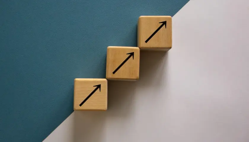 Trzy drewniane kostki tworzą schody, każda z czarną strzałką w górę. To symboliczne ten square games akcje, które rosną.