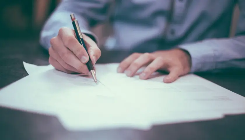 Dłoń pisze długopisem na papierze. To może być moment decyzji o porzuceniu pracy, podpisanie wypowiedzenia.