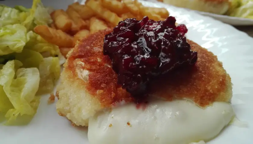 Pyszny camembert w panierce, z rozpływającym się serem, podany z frytkami i sałatką.