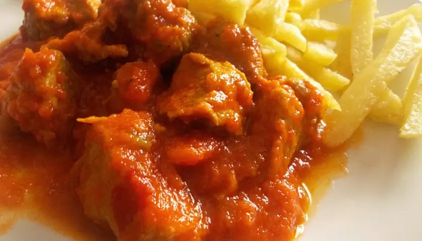 Sabroso carne de cerdo con tomate de la abuela, jugoso y tierno, acompañado de patatas fritas crujientes.
