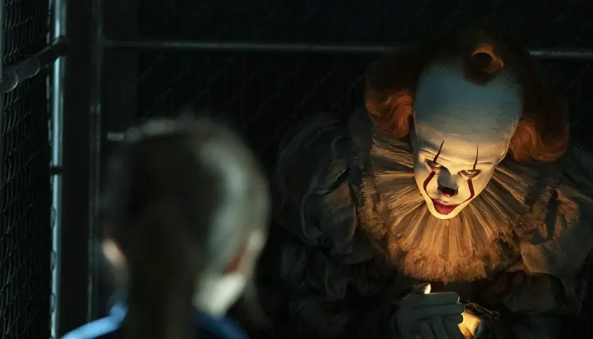 Przerażający klaun Pennywise z "To" w jednym z najlepszych horrorów ostatnich lat, świeci sobie zapalniczką.