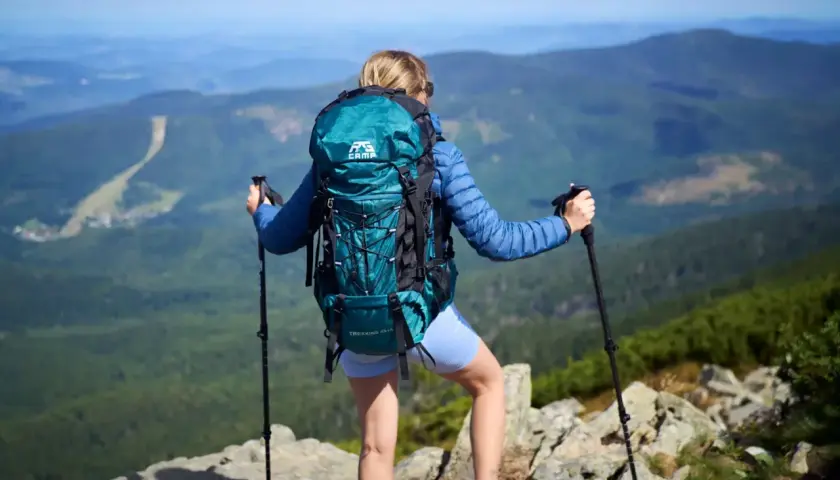 Kobieta z turkusowym plecakiem i kijkami trekkingowymi podziwia widok z góry. Idealny plecak turystyczny na wyprawę.