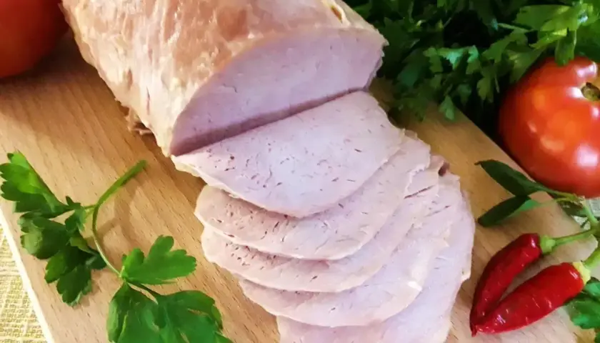 Pokrojony schab gotowany 2 razy po 10 minut, podany z pomidorami, papryczkami chili i natką pietruszki na desce.