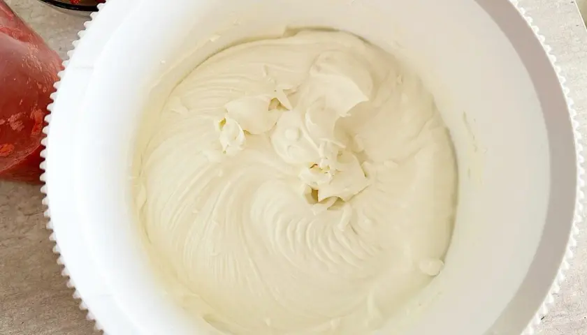 Gładki, puszysty krem z mascarpone w białej misie, gotowy do deseru. Obok miski widać truskawki.