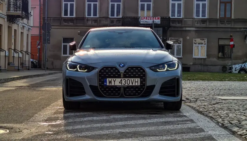 Szare BMW 420i z charakterystycznym grillem stoi na przejściu dla pieszych. W tle kamienice.