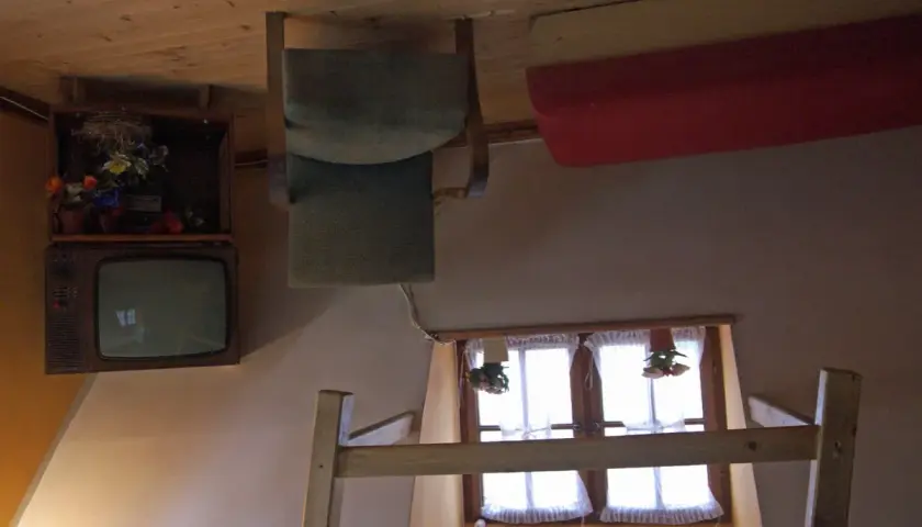 Wnętrze domu do góry nogami w Szymbarku: odwrócony telewizor, krzesło i łóżko.