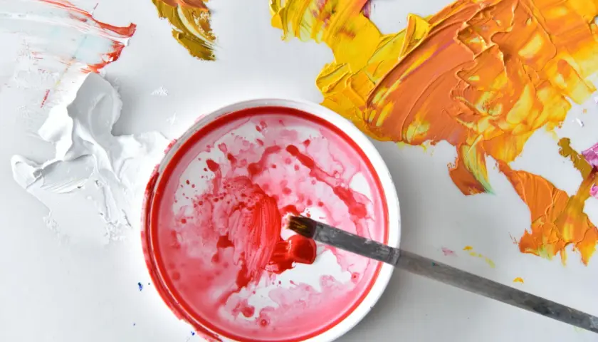 Pennello intinge nel rosso per capire come miscelare i colori per pittura murale. Macchie di giallo e arancio vibrante completano la scena.
