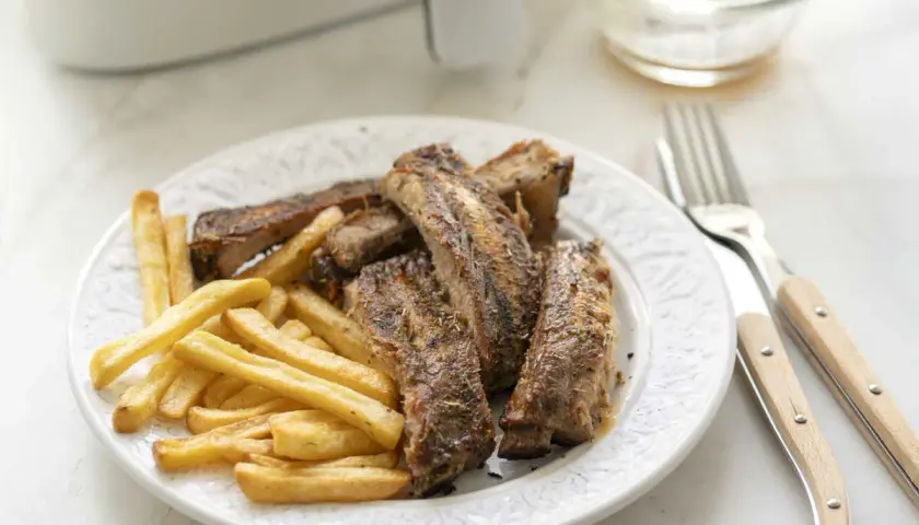 Costillas jugosas y patatas fritas crujientes, recién salidas de la freidora de aire. Un plato perfecto para disfrutar.