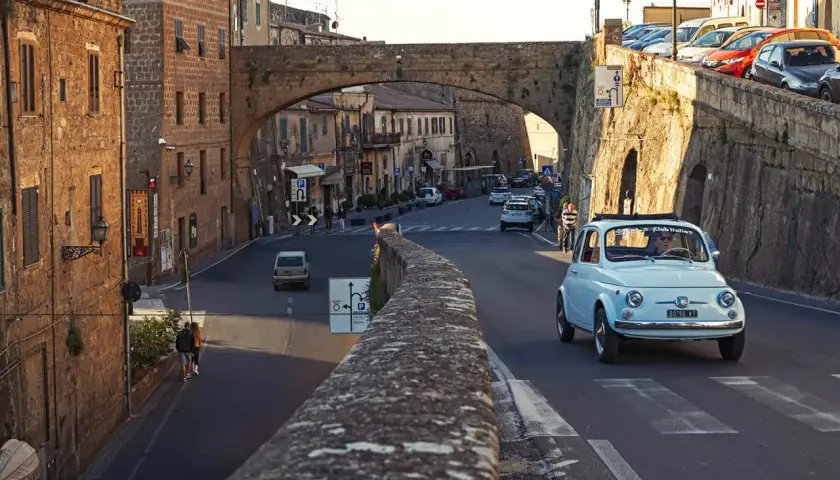A light blue Fiat 500 drives through a Tuscan town. Do you need a car in Florence to explore charming streets like this?