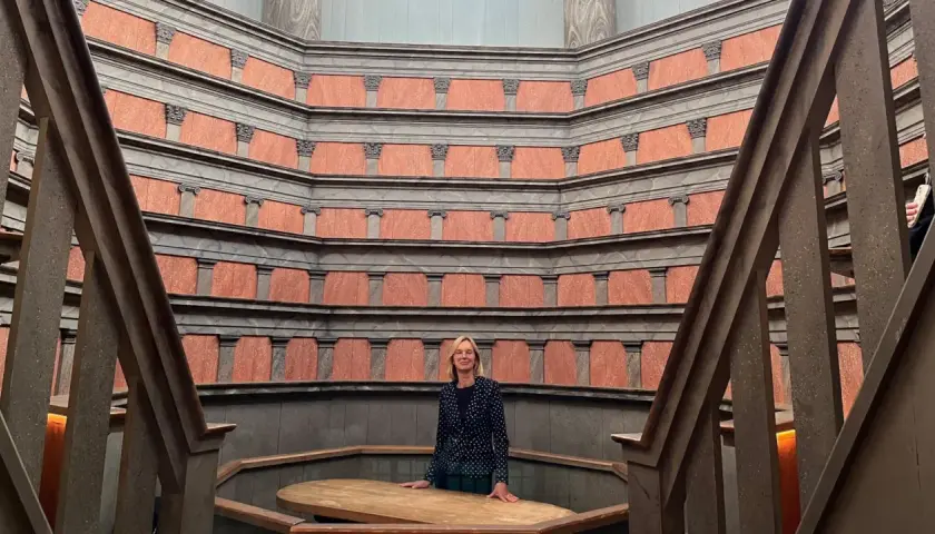 En kvinna står i den imponerande **anatomiska teatern Uppsala**. De rödbruna väggarna med sina pelare skapar en unik atmosfär.