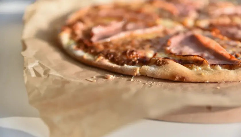Zbliżenie na pizzę z szynką na papierze do pieczenia.