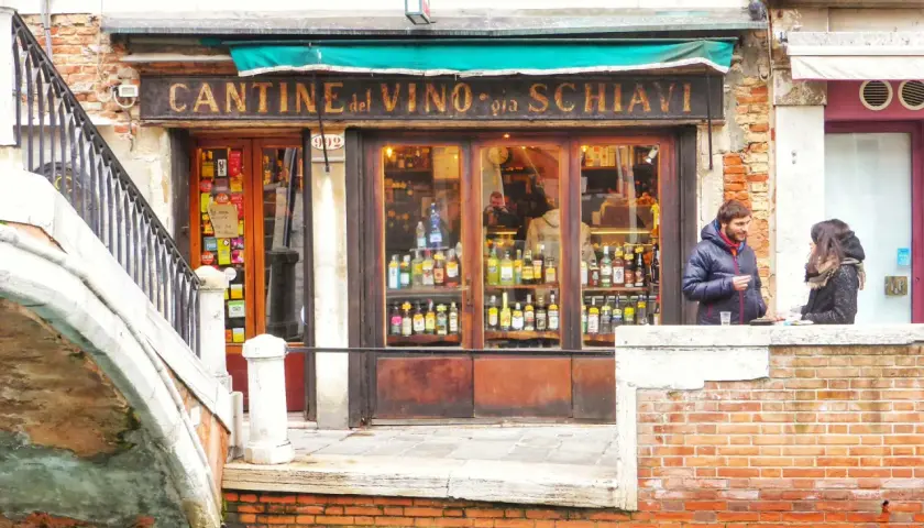 Cantina del Vino, un posto ideale per mangiare a Venezia spendendo poco. Coppia parla davanti al locale pieno di bottiglie.