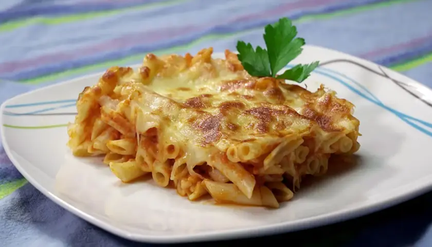 Porción de macarrones al horno gratinados con queso derretido y una hoja de perejil, servida en un plato blanco.