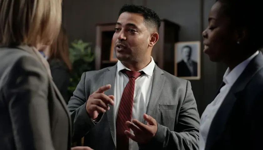 Un homme en costume explique avec passion à deux femmes, peut-être une affaire où ils risquent d'être déboutés en justice.