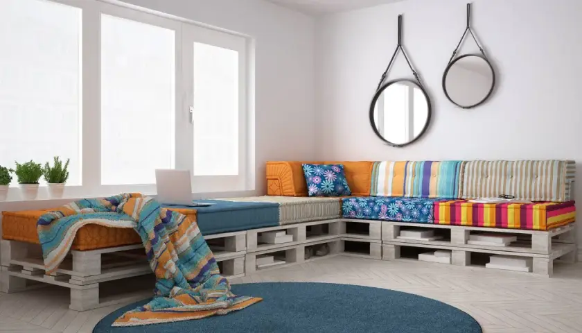 Divano con pallet, colorato e accogliente, con cuscini vivaci e una coperta morbida. Perfetto per un angolo relax.