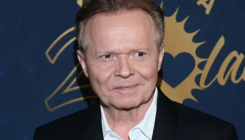 Michał Bajor w czarnym garniturze i białej koszuli, uśmiecha się. W tle złote napisy i serce.