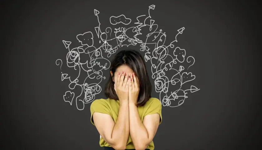 Donna con le mani sul viso, circondata da disegni caotici. Un'immagine che evoca la difficoltà nel come trattare un paranoico, con pensieri confusi e ansia.
