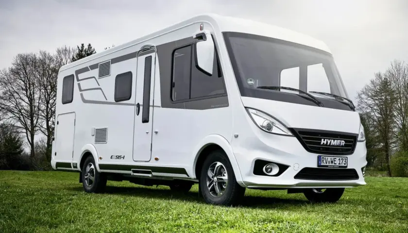 Biała kamper z serii Hymermobil, produkt Erwin Hymer Group, stoi na zielonej trawie.