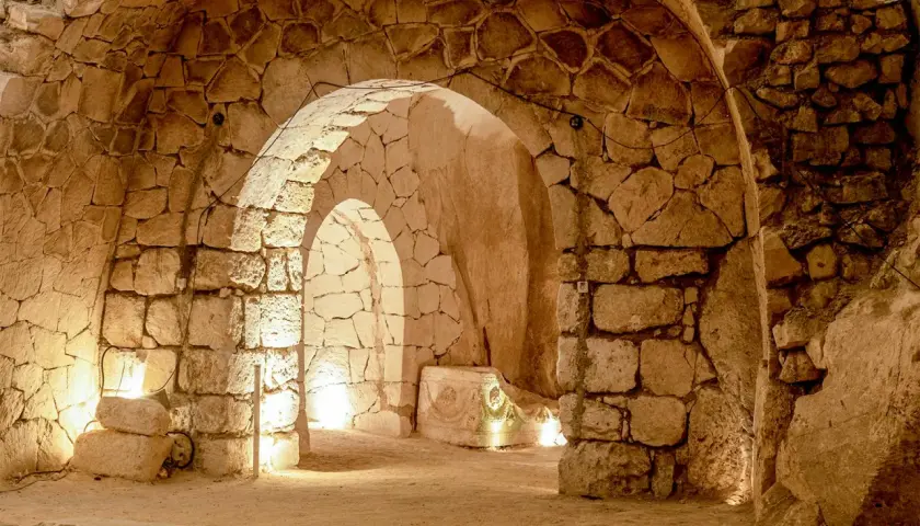 Intérieur voûté des catacombes Saint-Calixte, éclairé par des lumières douces, révélant des murs de pierres anciennes et un sarcophage orné.