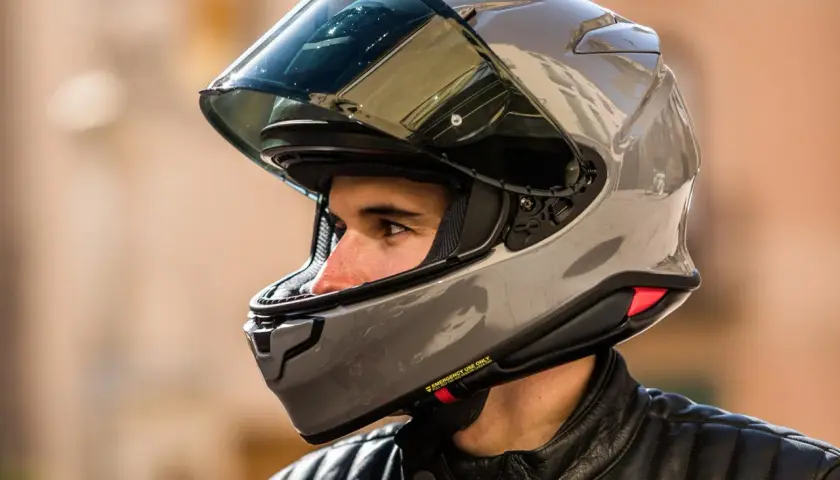 Hombre con casco moto 125 gris brillante, visor oscuro y chaqueta de cuero negra.