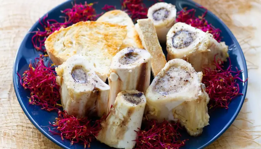 Pieczone szpik kostny wołowy z grzankami i kiełkami rzodkiewki na niebieskim talerzu.