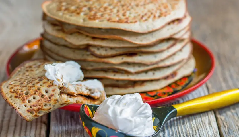 Pile de crêpes épaisses alsaciennes, garnies de crème fraîche. Une cuillère décorée en est aussi remplie.