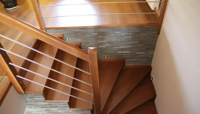 Eleganckie drewniane schody z metalową balustradą, prowadzące do górnego poziomu. Kamienna ściana stanowi stylowe tło, pokazując, jak zakończyć ostatni stopień schodów.