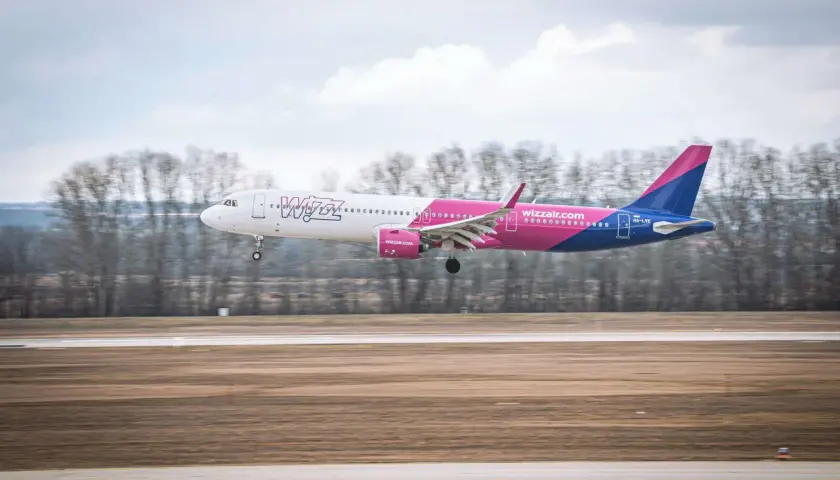 Samolot Wizz Air z różowym i niebieskim ogonem ląduje na pasie startowym.