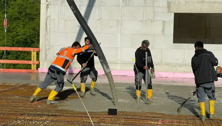 Arbeiter gießen Beton für die Bodenplatte. Sie schalen die Platte aus und verteilen den frischen Beton mit Werkzeugen.