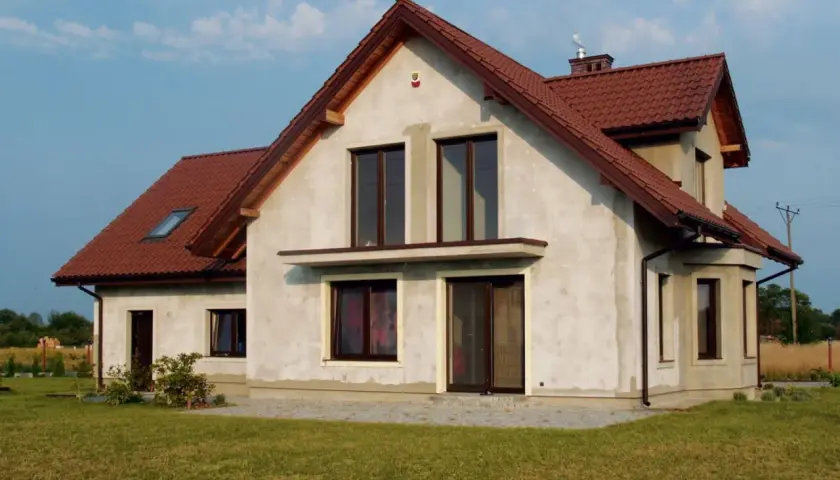 Dom w budowie z brązowym dachem, w tle linia wysokiego napięcia.