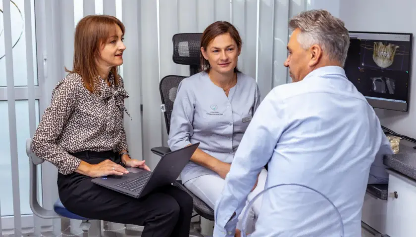 Pacjentka rozmawia z dentystką, która pokazuje jej zdjęcie rentgenowskie szczęki na laptopie.