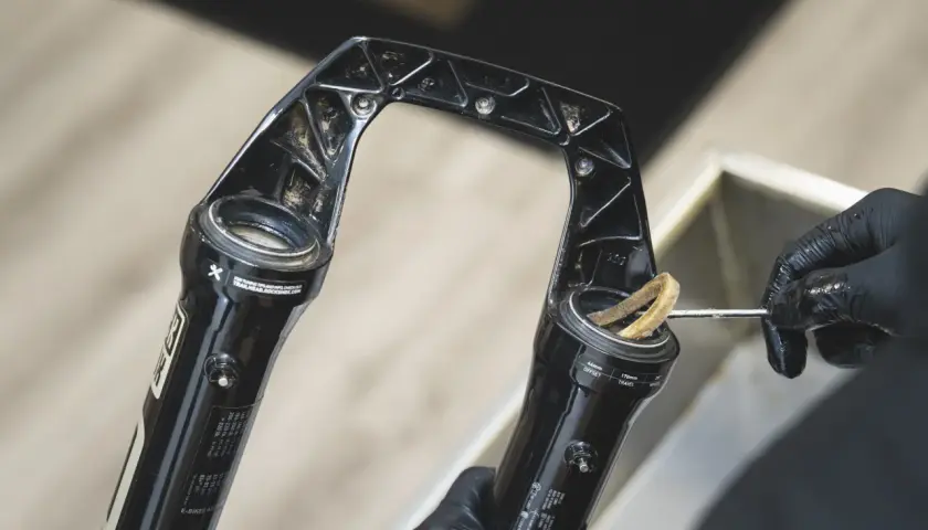 Gloved hands clean a RockShox Revelation RC fork, removing dirt from the stanchions.