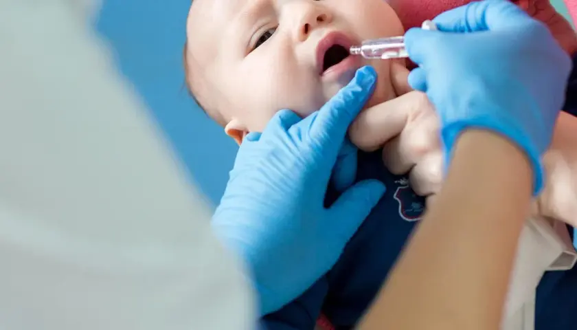 Ein Baby erhält Tropfen zur Vorbeugung von Rotavirus-Symptomen. Blaue Handschuhe schützen die Hände des Arztes.
