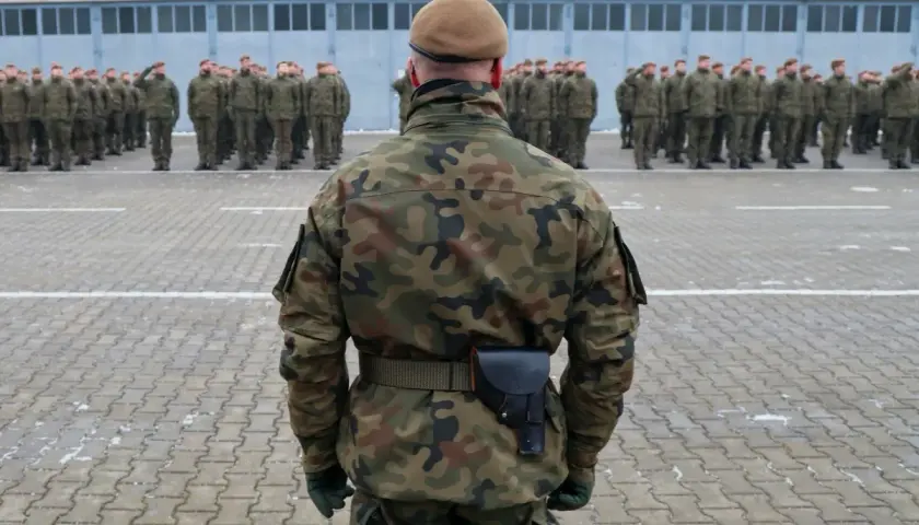 Żołnierz w mundurze polowym stoi na placu apelowym przed szeregiem innych żołnierzy. Czy w wieku 35 lat można iść do wojska? Tak, wiek nie jest przeszkodą.