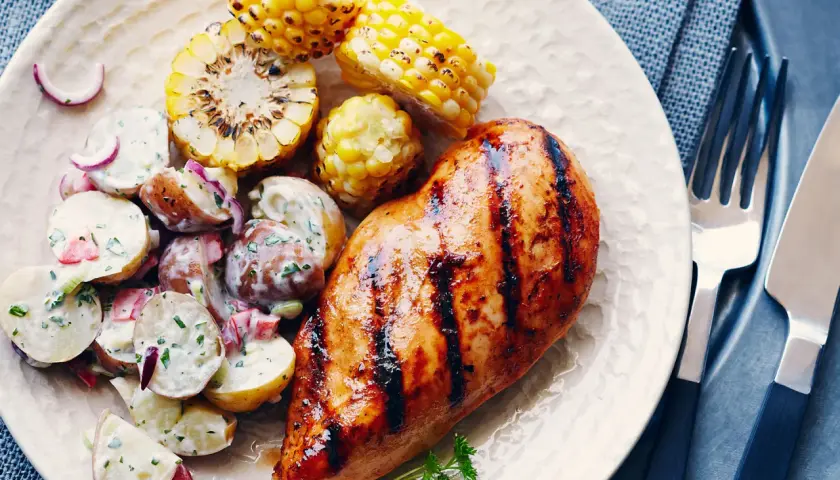 Un délicieux poulet grillé au sirop d'érable, servi avec une salade de pommes de terre crémeuse et des épis de maïs rôtis.