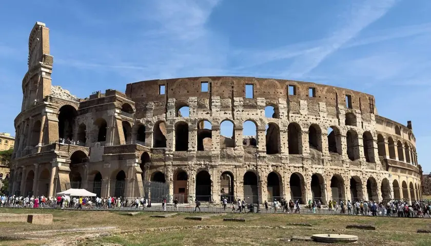 Il Colosseo, una delle principali attrazioni di Roma, 10 cose da vedere. Turisti ammirano l'anfiteatro romano sotto un cielo azzurro.