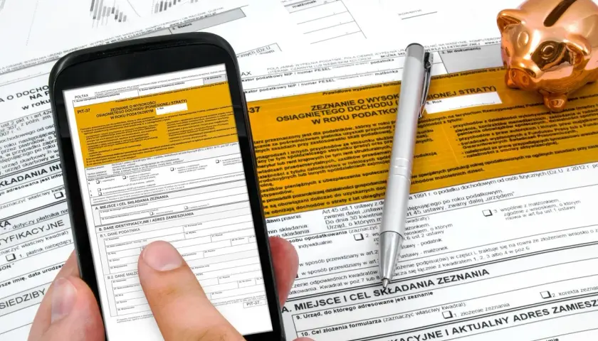 Smartfon z formularzem PIT-37 i złotą świnką skarbonką. Instrukcja jak rozliczyć PIT 37.