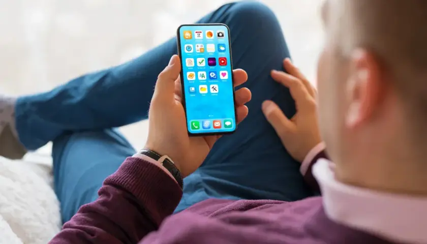 Dłoń trzyma smartfon z ikonami aplikacji. Szybkość ładowania telefonu zależy od wielu czynników, np. ładowarki i stanu baterii.